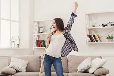 Happy young woman, cleaning, singing, and dancing at home.