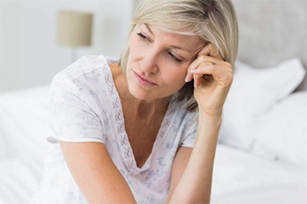 Woman sitting on a bed thinking.
