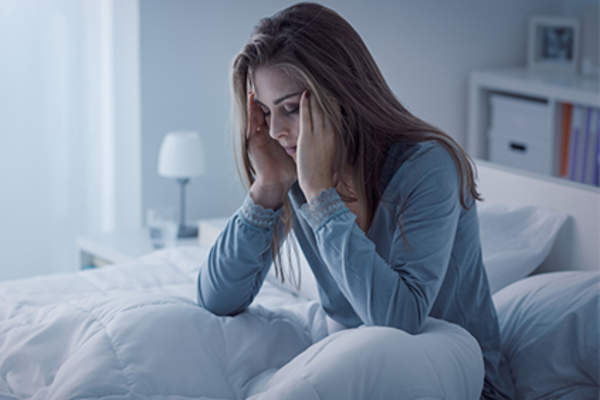 Young woman sitting up in bed feeling sick.