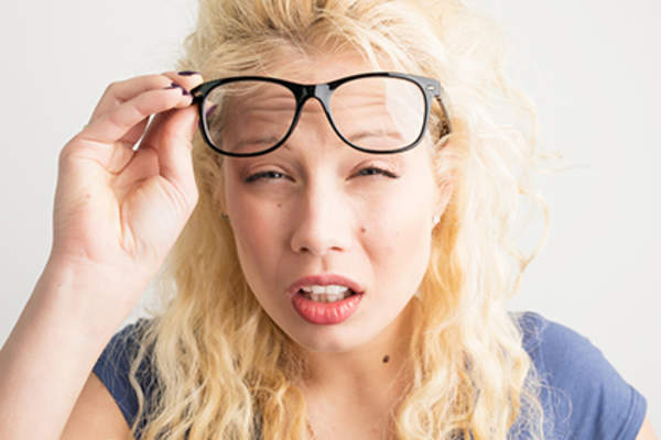 Woman with blurry vision lifting her glasses and squinting.