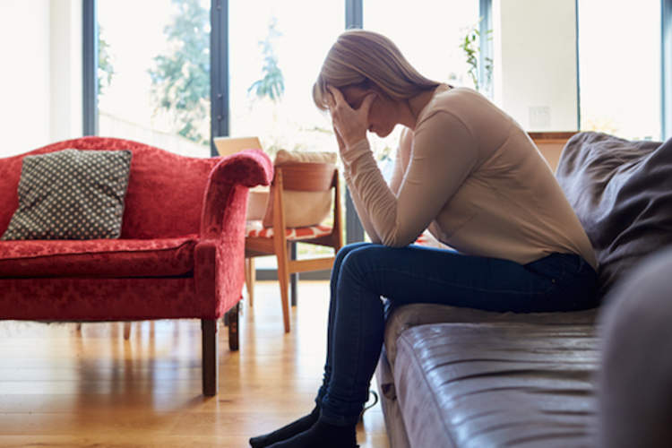 Depressed mature woman sitting on sofa at home.