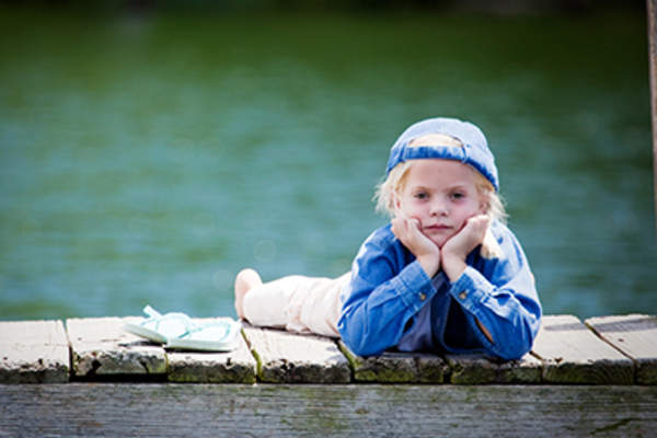 Unhappy child lying on a dock on a lake.