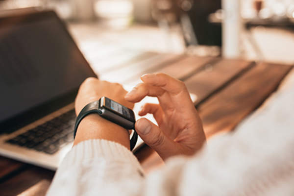 Woman using smartwatch at work on laptop.