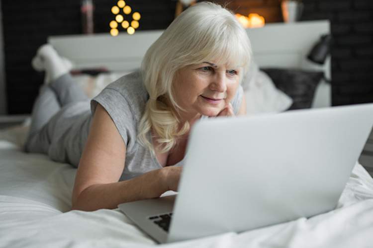 Older woman in bedroom on computer.