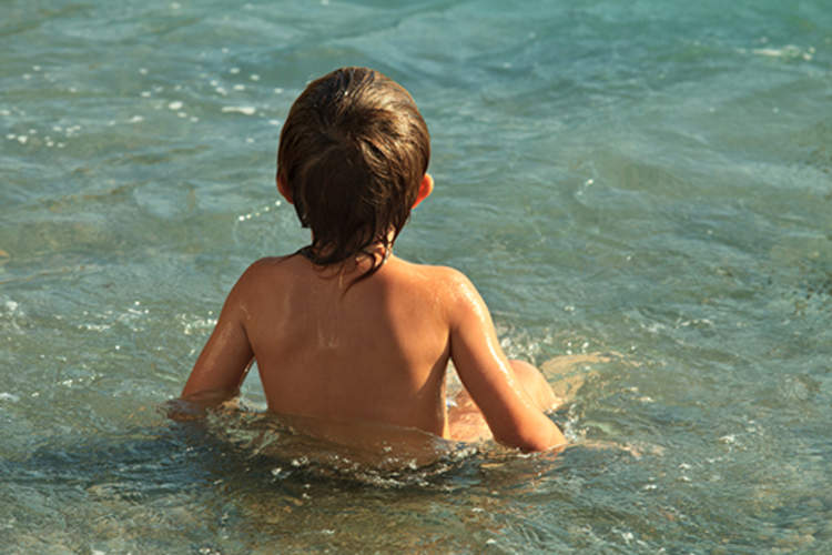 young boy sitting in ocean water at the beach image