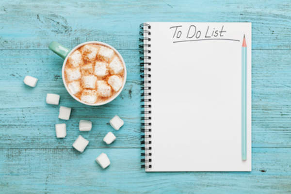 To do list notebook next to a cup of hot cocoa.