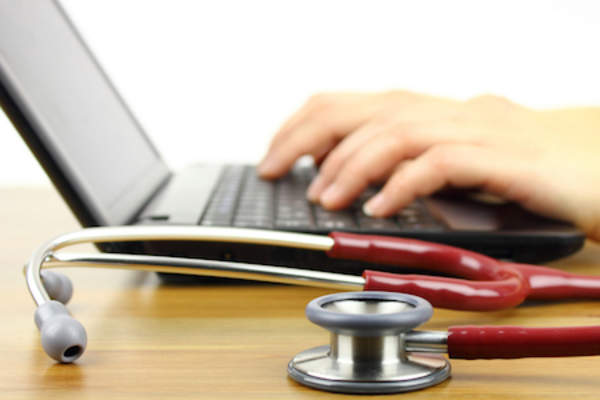 Hands working on laptop with stethoscope.