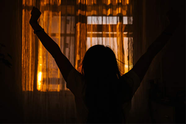 Woman stretching sitting on bed waking up at sunrise.