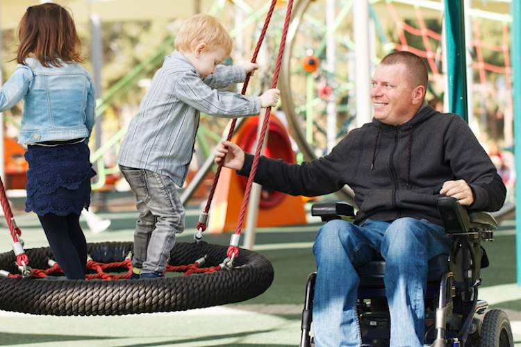 Man in wheelchair at playground with children.