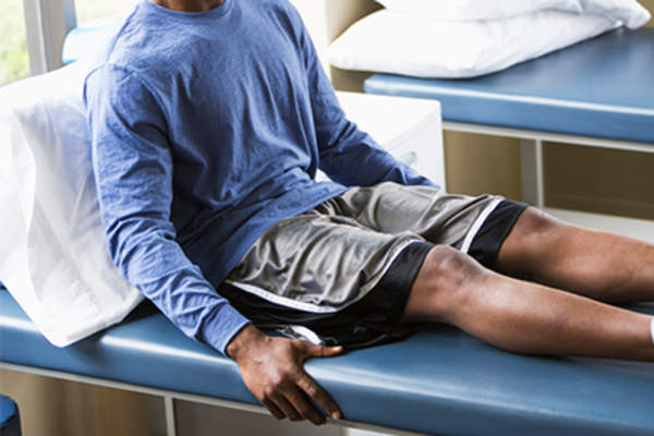 Man in basketball shorts sitting on exam table.
