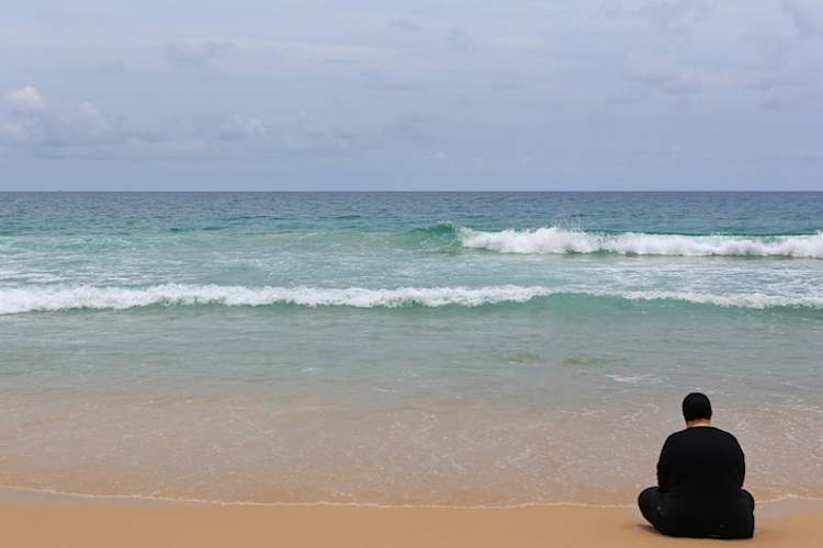 Lonely woman sitting on empty beach.