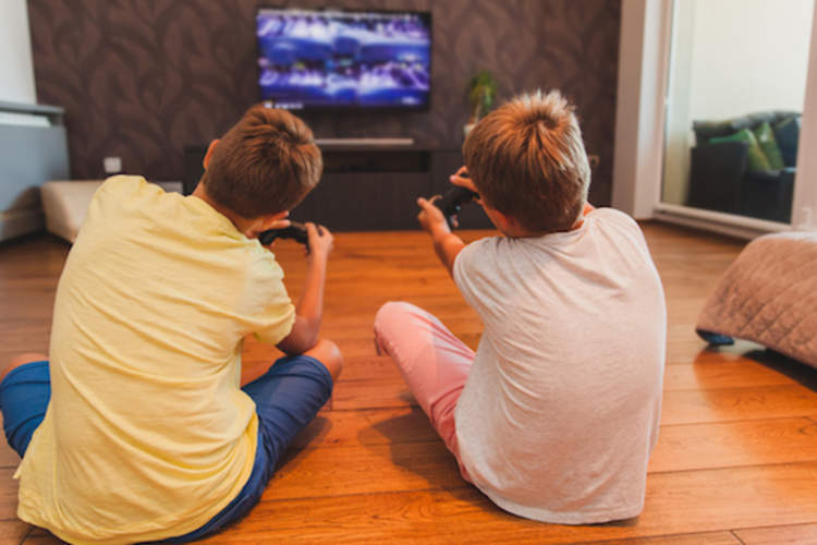 Two boys playing video game, sitting on floor in living room.