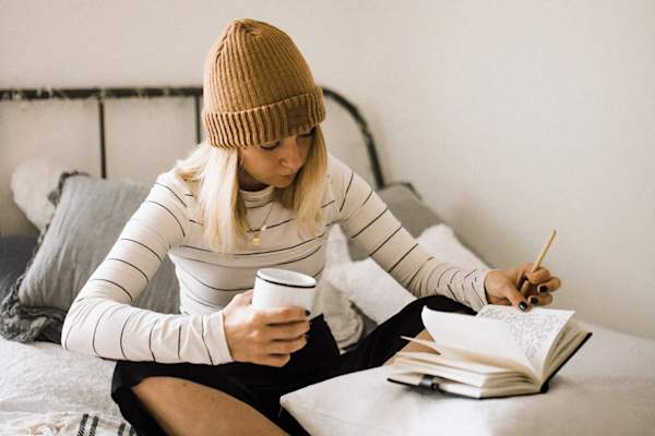 woman writing in journal on bed