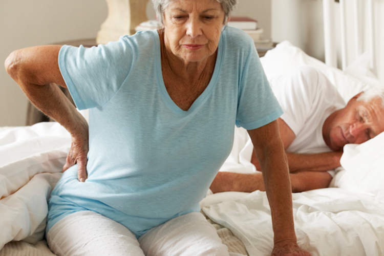 A woman with spinal stenosis back pain gets out of bed.
