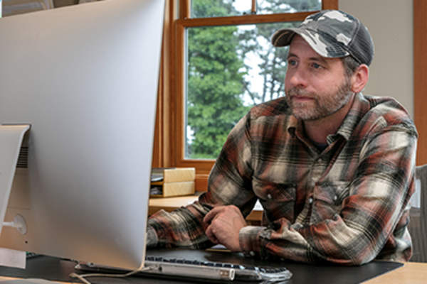 Man working at a desk while wearing a baseball cap.