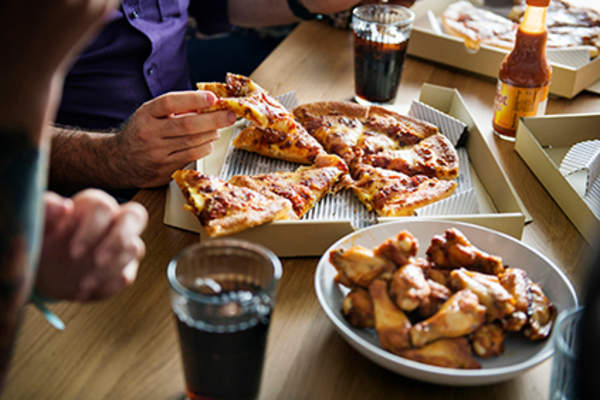 Family eating chicken wings, pizza, and soda.