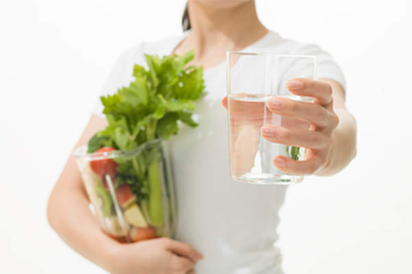 Woman holding glass of water and bag of vegetables.