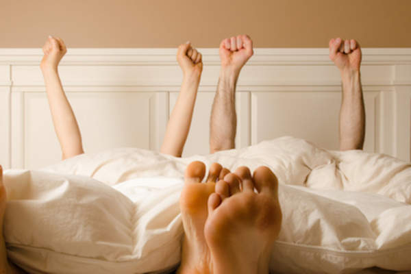 Couple in bed arms up in celebration.