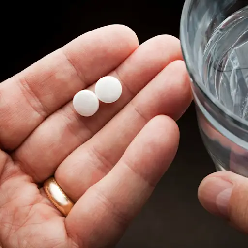 Hands holding two aspirin and a glass of water