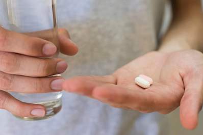 Hand holding two pills and glass of water