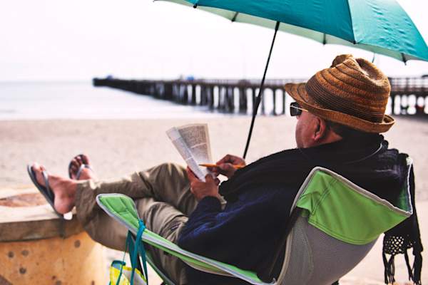senior man reading on beach wearing sun-protecting clothes
