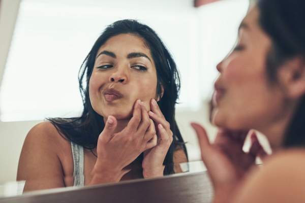 woman popping pimple in mirror