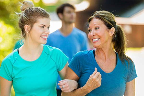 Smiling mother and teen daughter walking with arms linked.