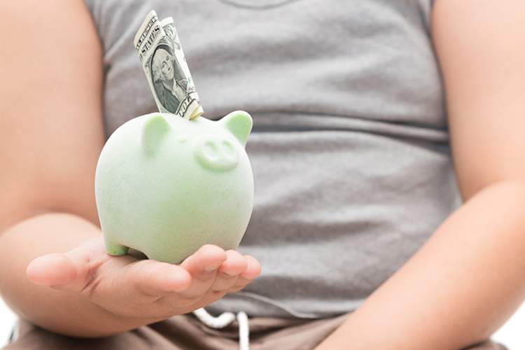 An obese woman holds a piggy bank with dollars in it.