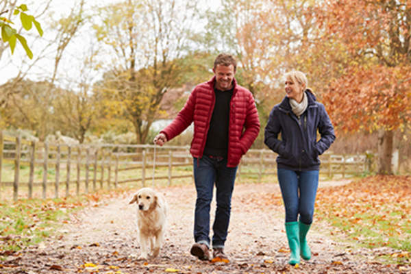Man and woman taking walk with dog in fall.