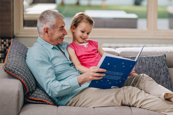 Grandfather reading to young granddaughter on the couch.