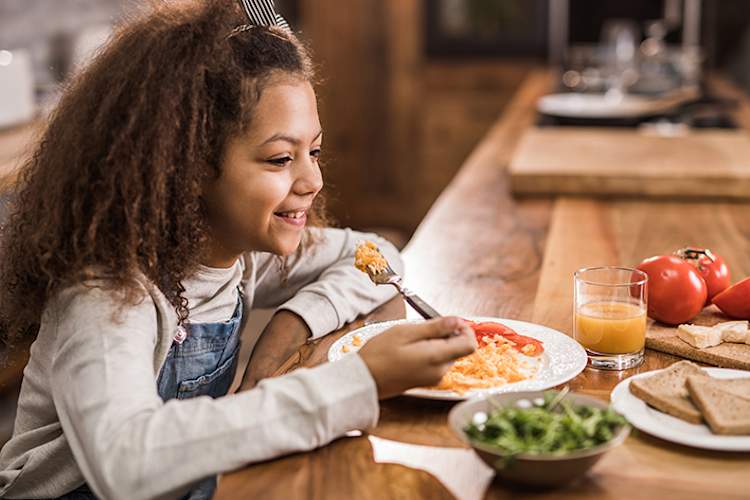 Young girl eating eggs with a well-balanced breakfast.