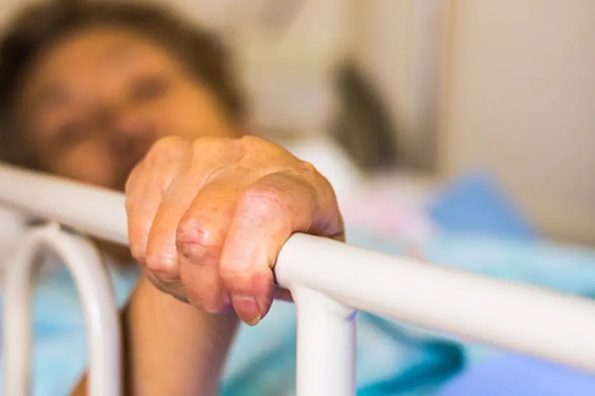 Elderly woman in hospital bed holding onto bed rail.