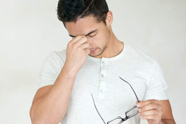 Young man holding eye glasses rubbing eyes.