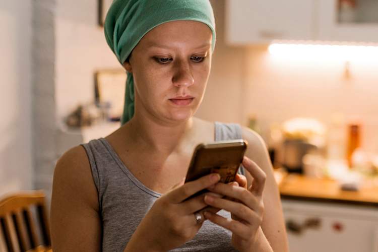 Young woman with cancer on cellphone in kitchen at home.