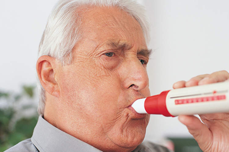 Senior man blowing into a spirometer for a spirometry test.