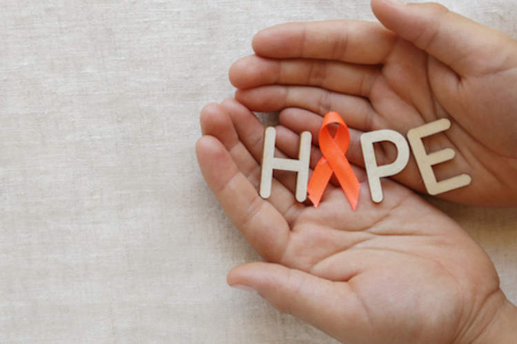Multiple sclerosis awareness ribbon in cupped hands with wooden letters spelling out "HOPE".