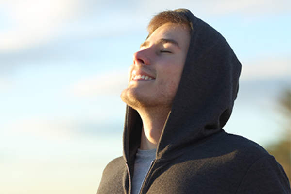 Smiling young man in the sun with eyes closed.
