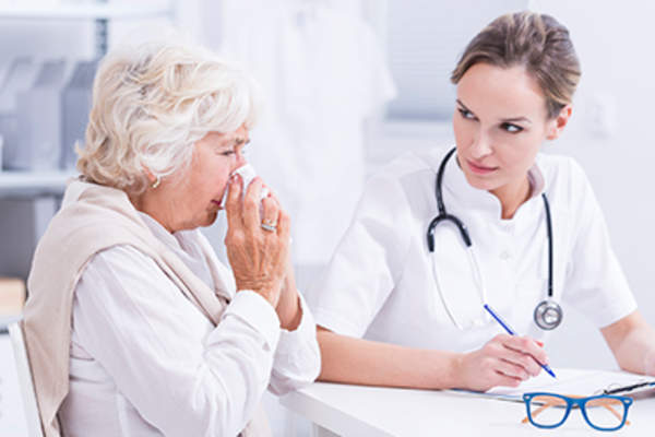 Senior woman blowing her nose in a doctor's office.