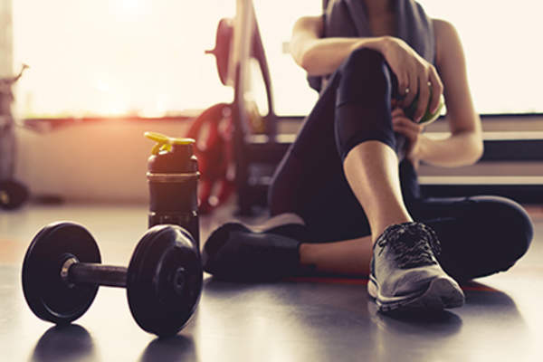 Woman sitting in a gym next to a dumbbell.