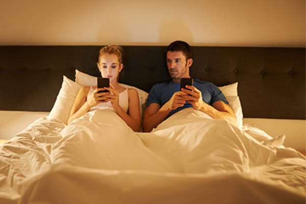 Couple in bed on phones, jealousy or paranoia.