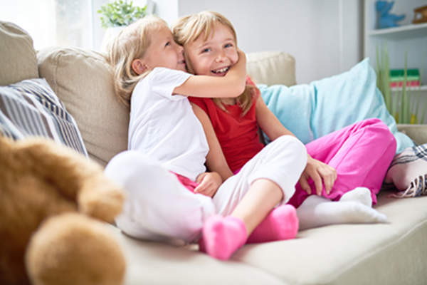 Young sisters smiling and hugging on couch.