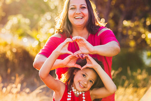 Woman and young girl smiling and making heart symbols with hands.