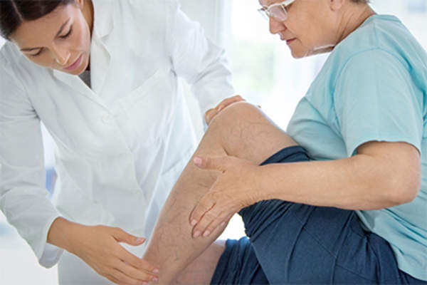 Doctor examining the skin on an older woman's lower leg.