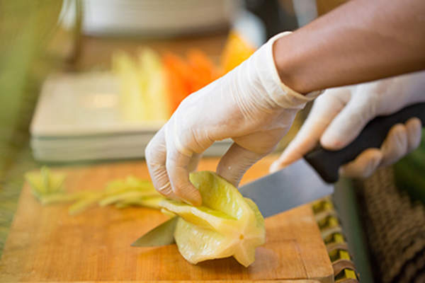 Cutting fruit with gloves on a cutting board.