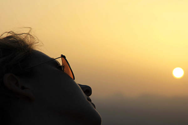 Woman wearing sunglasses looking toward sun at sunset.
