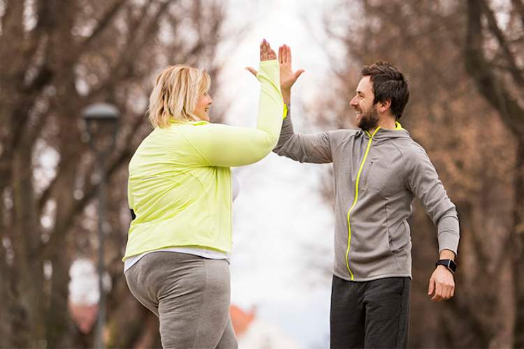 Trainer high fives an overweight woman exercising in the park.