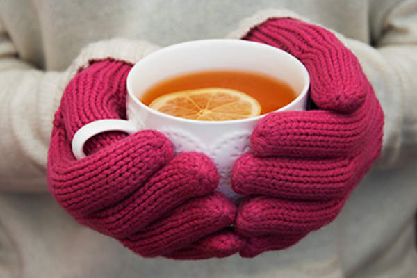 Woman wearing hot pink gloves and holding a mug of tea.