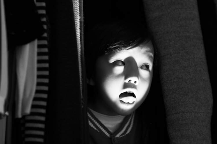 Child hiding in closet making scary faces.