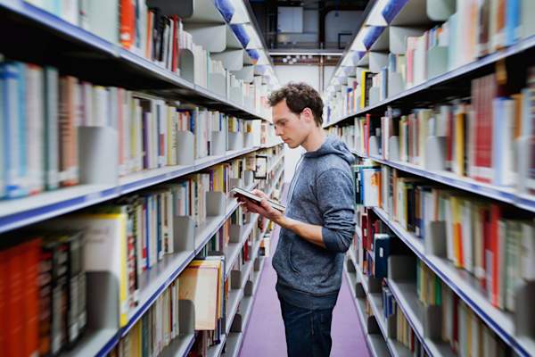 Young man in library examining book.