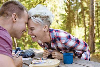 Man and woman playing cards on picnic table while camping.
